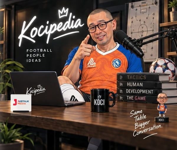 Koci di meja siaran Kocipedia: laptop, mug, tumpukan buku, bola, dan mikrofon